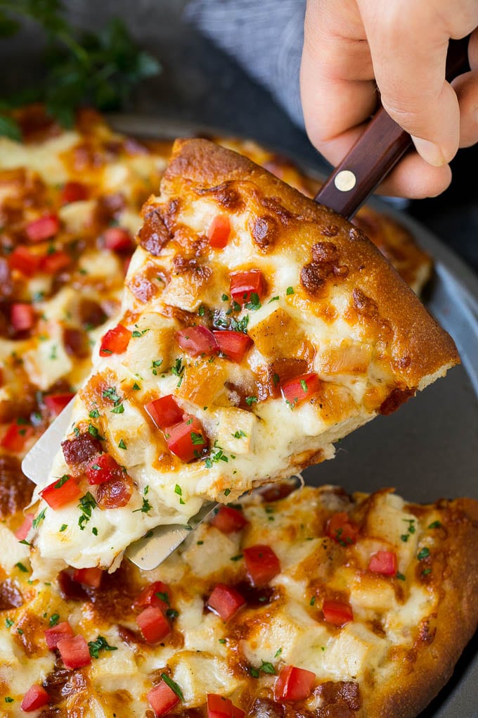 Chicken Alfredo Pizza Recipe #pizza #chicken #bacon #dinner #ezlod A hand holding a spatula with a piece of chicken Alfredo pizza on it.