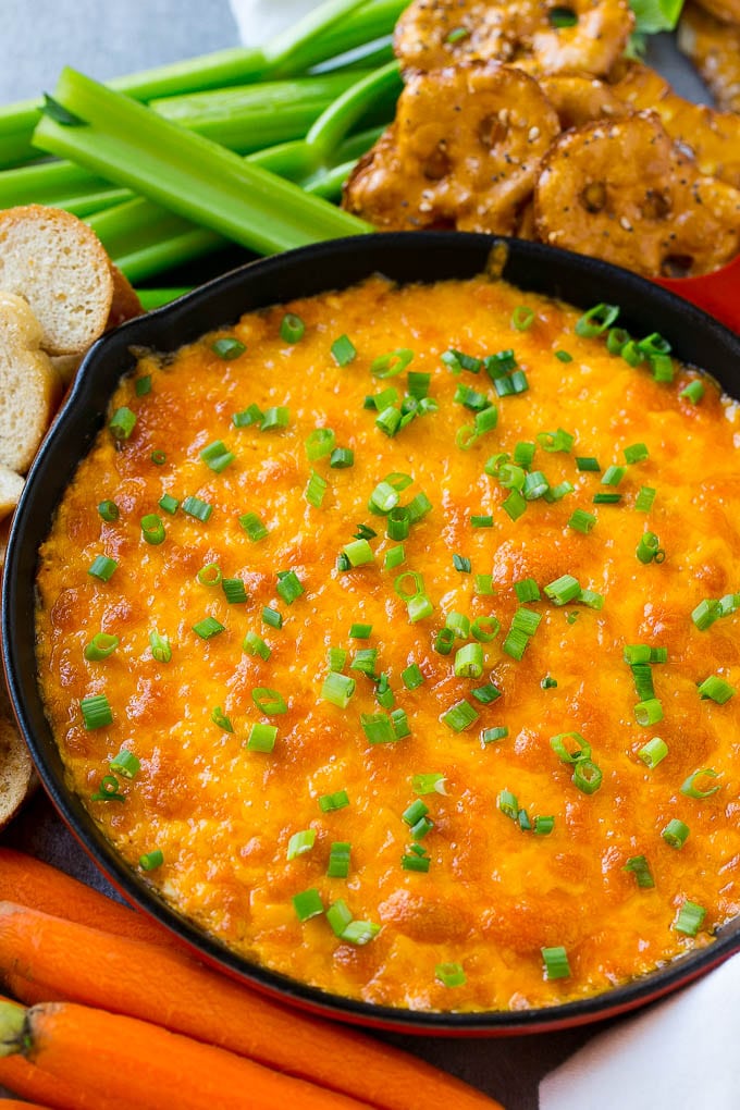 Buffalo Ranch Chicken Dip | Buffalo Chicken Dip | Baked Buffalo Dip | Cheesy Buffalo Dip #buffalowings #buffalochicken #dip #lowcarb #appetizer #ezlod Buffalo ranch chicken dip topped with melted cheese and green onions, surrounded by vegetables, pretzels and baguette slices.