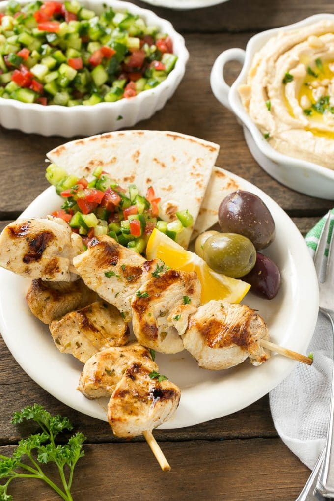Greek Chicken Souvlaki Recipe | Easy Greek Chicken | Chicken Souvlaki | Greek Chicken Skewers | Easy Greek Chicken Skewers #chicken #kabobs #glutenfree #keto #lowcarb #grilling #ezlod A plate of skewers with olives and pita bread.