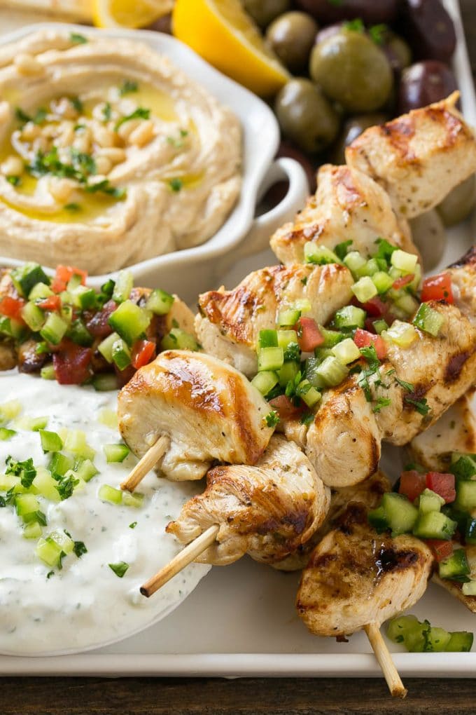 Greek Chicken Souvlaki Recipe | Easy Greek Chicken | Chicken Souvlaki | Greek Chicken Skewers | Easy Greek Chicken Skewers #chicken #kabobs #glutenfree #keto #lowcarb #grilling #ezlod A tray of chicken souvlaki kabobs with olives, hummus, pita bread and yogurt sauce.