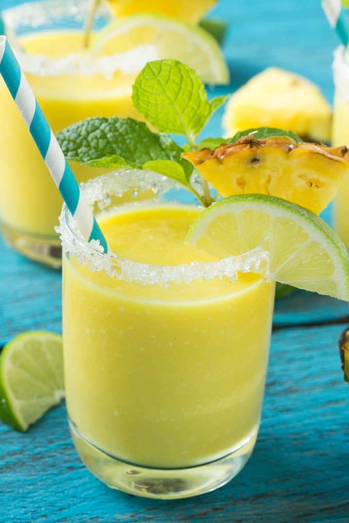 Pineapple Coconut Smoothie Recipe |Tropical Smoothie | Pineapple Smoothie #smoothie #pineapple #coconut #healthy #cleaneating #ezlod A cup of pineapple smoothie with garnishes of lime, pineapple wedges and mint sprigs.