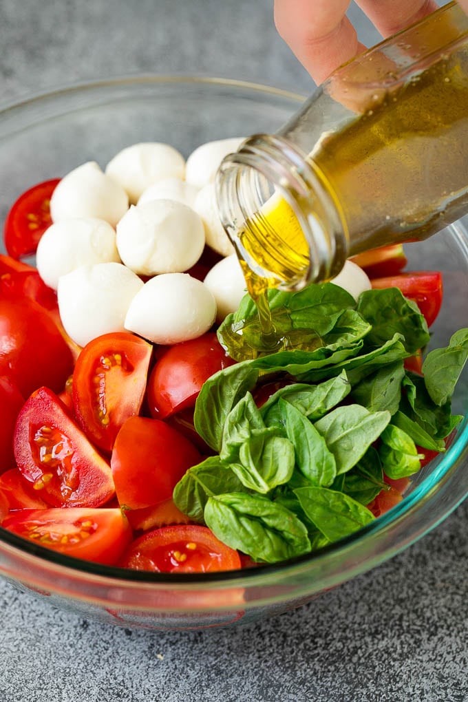 Caprese Salad Recipe | Tomato Salad #salad #tomato #mozzarella #cheese #basil #caprese #summer #ezlod Olive oil being poured over tomatoes, mozzarella and basil leaves.