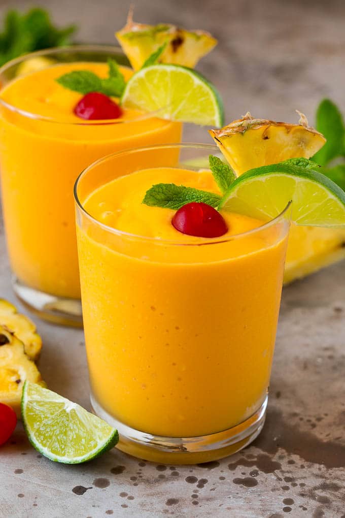 Tropical Smoothie Recipe | Mango Smoothie | Pineapple Smoothie #smoothie #mango #pineapple #banana #drink #ezlod Two tropical smoothies with fresh mint, lime wedges and sliced pineapple.