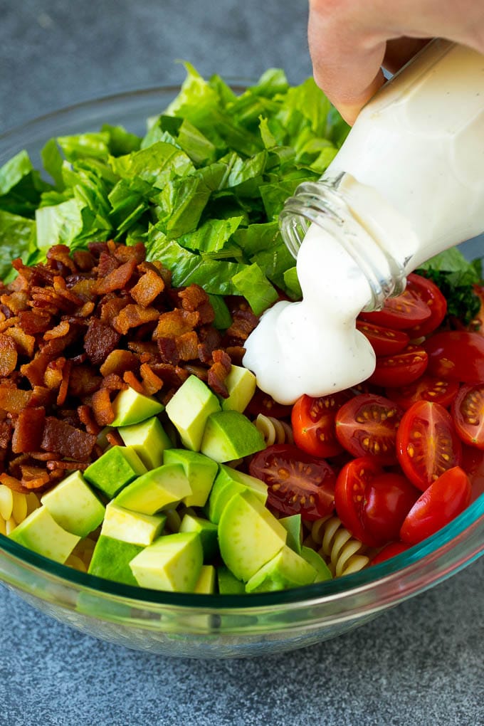 BLT Pasta Salad Recipe | Easy Pasta Salad | Bacon Pasta Salad #salad #pasta #blt #bacon #avocado #dinner #ezlod Ranch dressing being poured over tomatoes, lettuce, bacon and avocado.