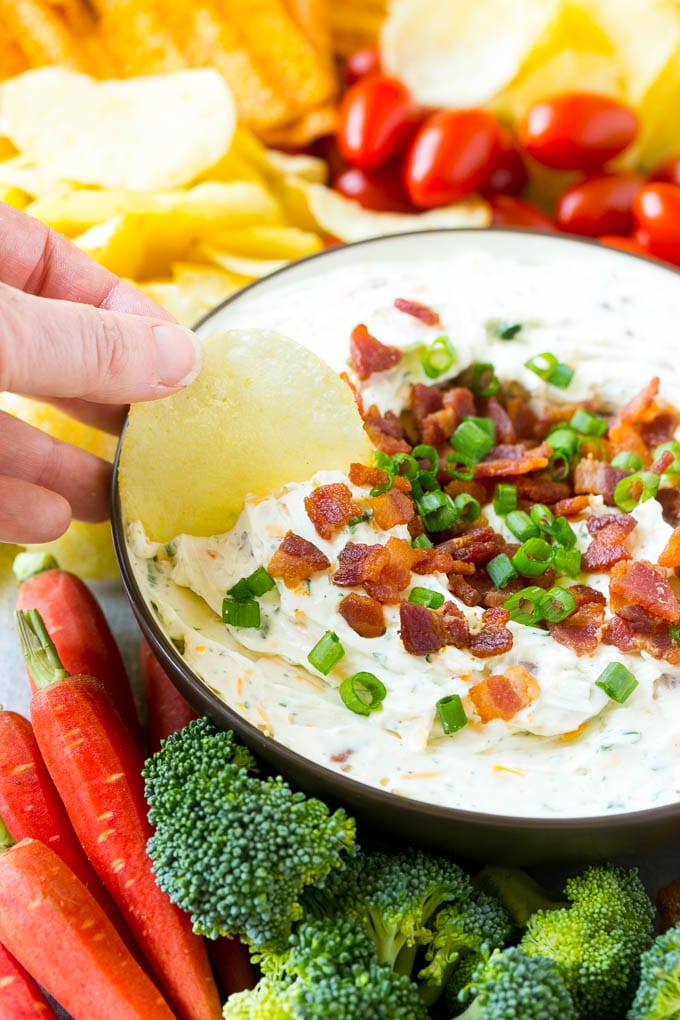 Bacon Ranch Dip Recipe | Homemade Ranch Dip | Easy Dip Recipe | Cheddar Ranch Dip #ranch #ranchdip #bacondip #dip #snack #ezlod #baconranchdip A hand scooping up bacon ranch dip with a potato chip.