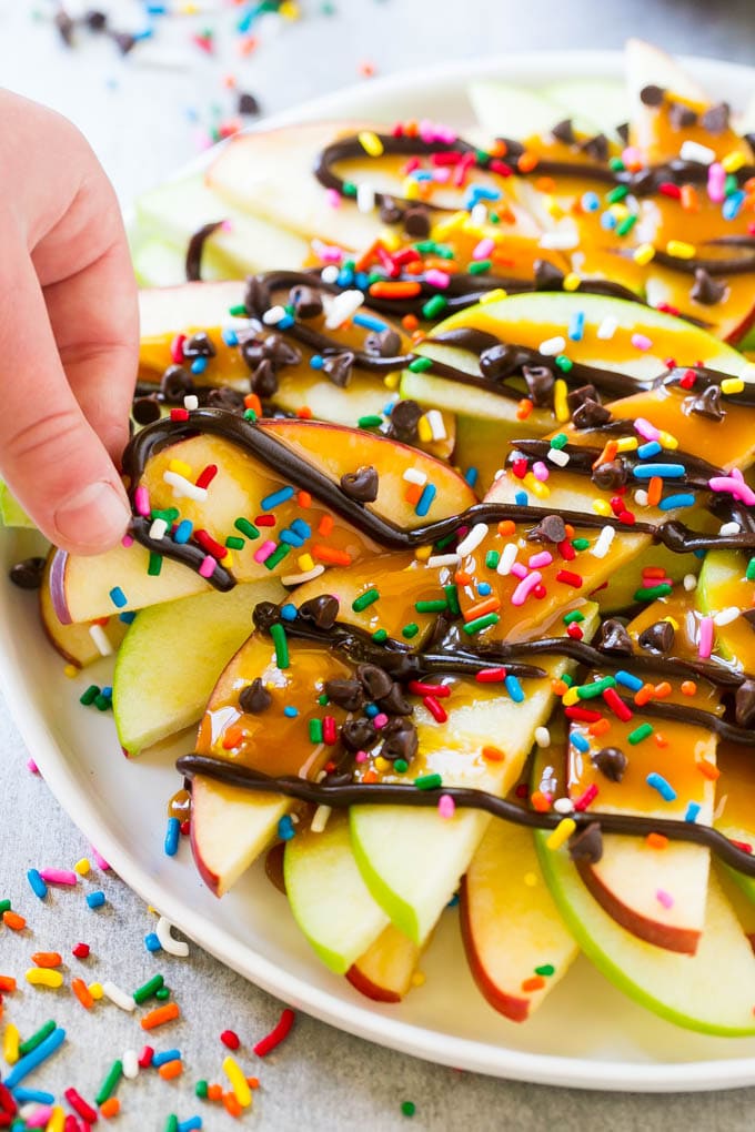 Apple Nachos Recipe | After School Snack | Caramel Apples #apple #apples #caramelapple #snack #dessert #ezlod A plate of caramel apple nachos with a hand reaching out to take one.
