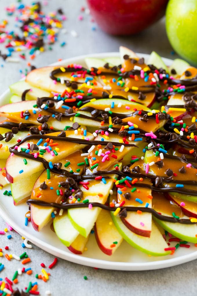 Apple Nachos Recipe | After School Snack | Caramel Apples #apple #apples #caramelapple #snack #dessert #ezlod A plate of red and green sliced apples drizzled with caramel and chocolate, then topped with rainbow sprinkles and chocolate chips.