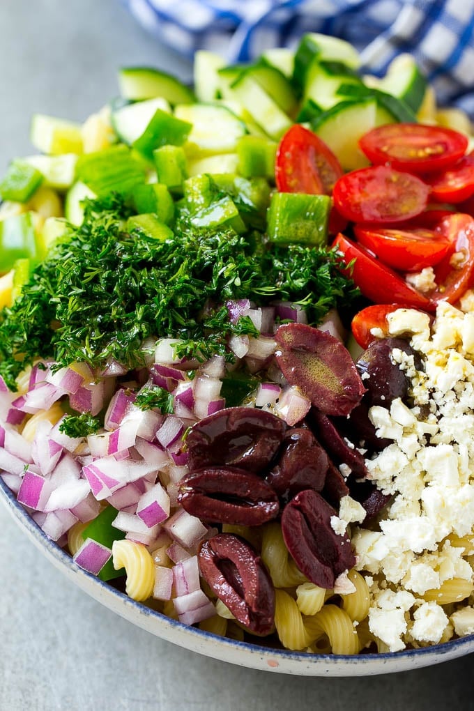 Greek Pasta Salad | Easy Pasta Salad | Vegetable Pasta Salad #pasta #salad #greek #cucumber #tomato #vegetarian #dinner #ezlod A bowl of pasta with red onion, kalamata olives, bell pepper and tomatoes, with a drizzle of Greek dressing.