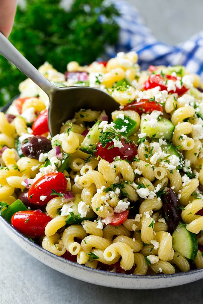 Greek Pasta Salad | Easy Pasta Salad | Vegetable Pasta Salad #pasta #salad #greek #cucumber #tomato #vegetarian #dinner #ezlod A bowl of Greek pasta salad with a serving spoon in it.