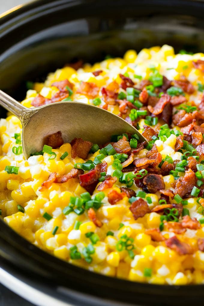 Slow Cooker Creamed Corn Recipe | Easy Creamed Corn Recipe | Slow Cooker Creamed Corn with Bacon | Southern Creamed Corn | Creamed Corn with Cream Cheese #creamedcorn #corn #bacon #crockpot #slowcooker #dinner #ezlod A serving spoon in a crock pot full of creamed corn.