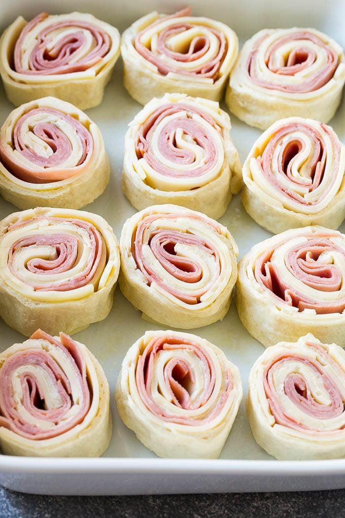 Ham and Cheese Pinwheels Recipe | Ham and Cheese Roll Ups | Ham and Cheese Rolls | Ham and Cheese Bread Rolls #ham #cheese #appetizer #pinwheels #ezlod Rolled up ham, cheese and pizza dough circles in a baking dish.