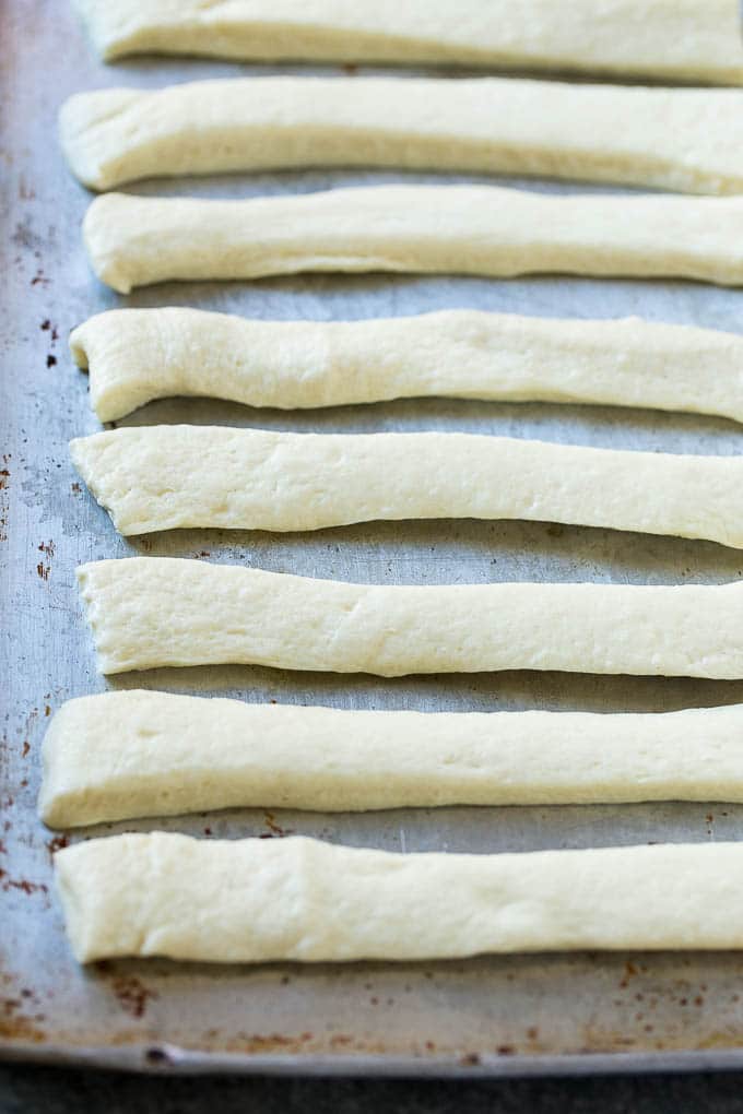 Garlic Knots Recipe | Garlic Rolls | Garlic Butter Rolls | Garlic Bread Recipe #garlic #garlicbread #garlicknots #breadsticks #ezlod Strips of pizza dough on a sheet pan that are ready to be tied up.