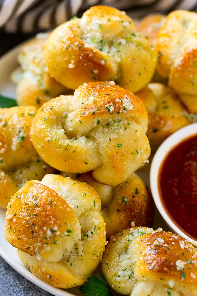 Garlic Knots Recipe | Garlic Rolls | Garlic Butter Rolls | Garlic Bread Recipe #garlic #garlicbread #garlicknots #breadsticks #ezlod A plate of garlic knots slathered in butter next to a cup of marinara sauce.