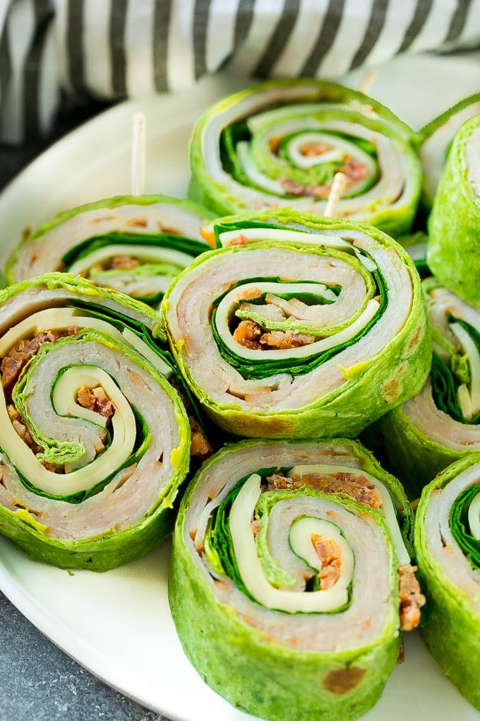 Turkey Roll Ups Recipe | Turkey Pinwheel Sandwiches | Turkey Roller Sandwiches #turkey #avocado #sandwich #lunch #appetizer #ezlod Turkey roll up sandwiches filled with cheese, avocado, bacon, turkey and spinach and stacked on a plate.