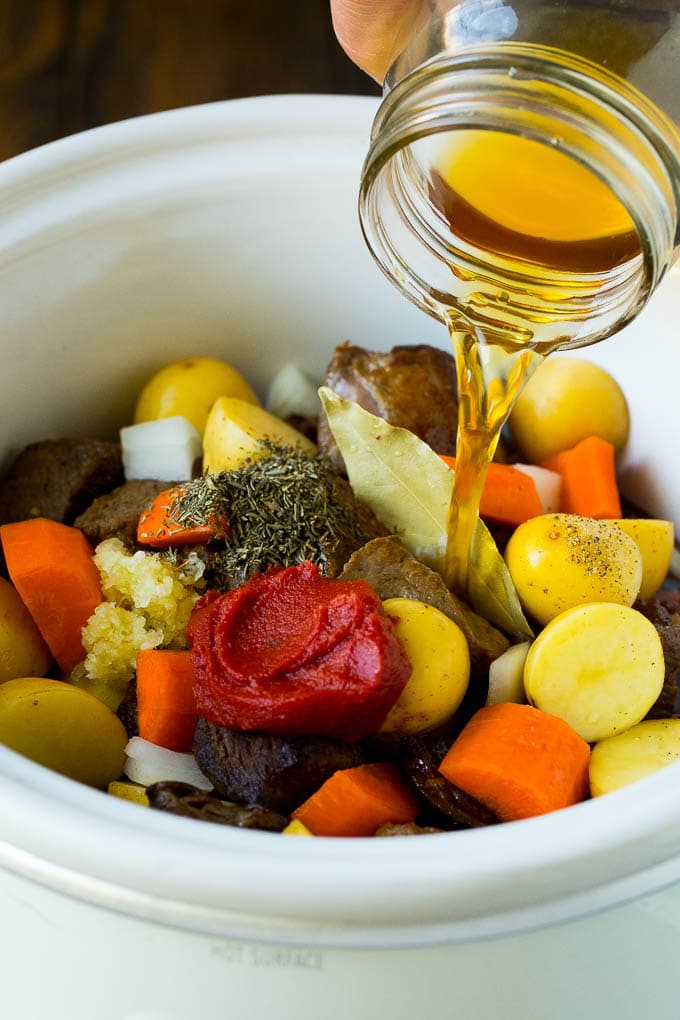 Slow Cooker Beef Stew Recipe | Crockpot Beef Stew #stew #soup #beef #slowcooker #crockpot #dinner #ezlod Broth being poured into a slow cooker filled with beef and vegetables.