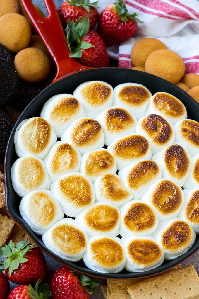 S'mores Dip Recipe | S'mores Skillet | Baked S'mores #smores #dip #chocolate #marshmallow #dessert #ezlod A skillet of s'mores dip with melted chocolate chips and toasted marshmallows, surrounded by graham crackers, cookies and strawberries.