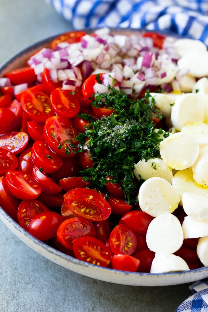 Cherry Tomato Salad Recipe | Tomato Mozzarella Salad | Caprese Salad | Tomato Salad #tomatoes #salad #tomatosalad #caprese #ezlod Cherry tomatoes, herbs, mozzarella balls and red onion drizzled with dressing in a bowl.