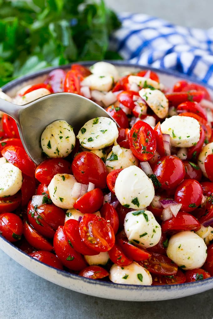 Cherry Tomato Salad Recipe | Tomato Mozzarella Salad | Caprese Salad | Tomato Salad #tomatoes #salad #tomatosalad #caprese #ezlod A bowl of cherry tomato salad with a serving spoon in it.