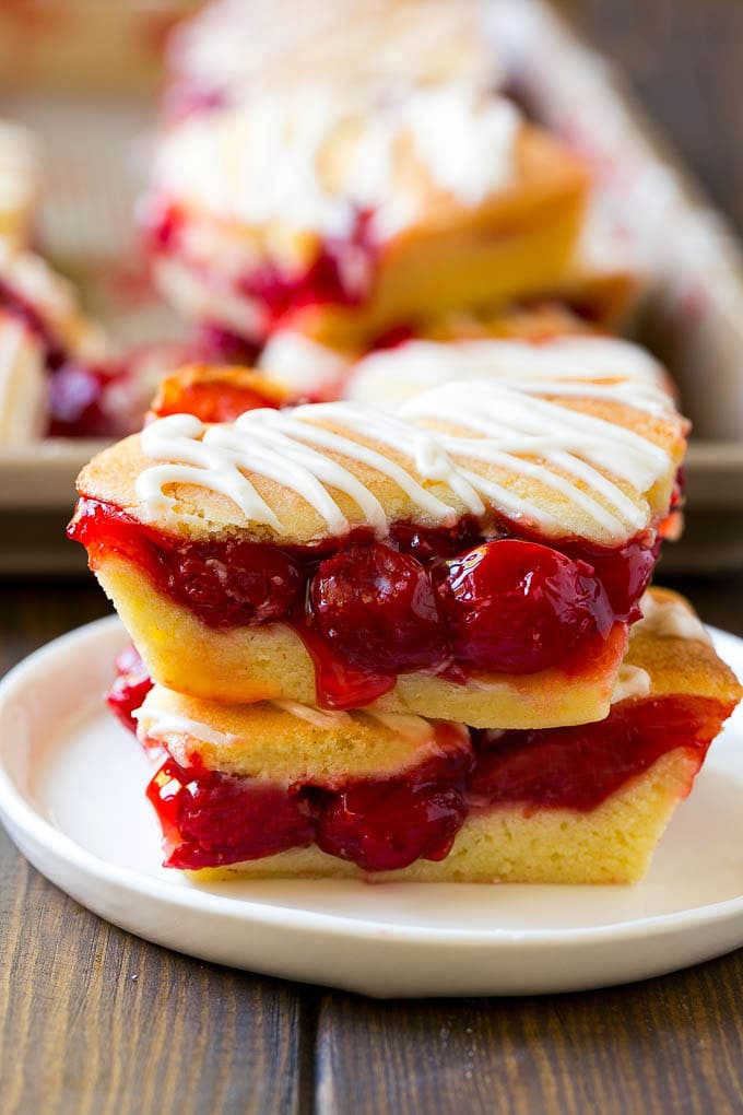 Cherry Bars Recipe | Cherry Pie Bars | Cherry Cookies | Bar Cookies #cookies #bars #cherry #baking #dessert #sweets #ezlod Two cherry bars on a plate with a pan of bars in the background.