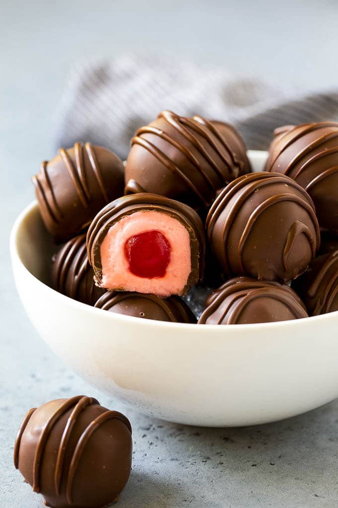 Chocolate Covered Cherries Recipe | Cherry Cordials | Cherry Candy #chocolate #candy #dessert #cherry #sweets #ezlod A bowl of chocolate covered cherries with one cut open.