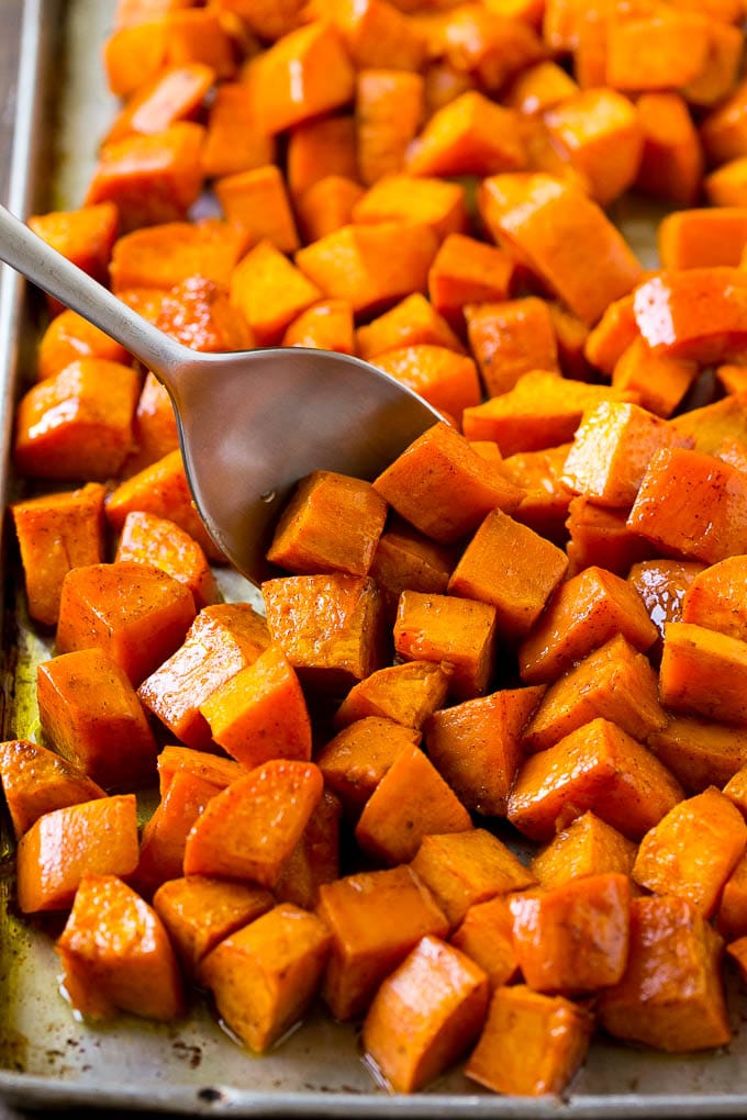 Maple Roasted Sweet Potatoes Recipe | Easy Sweet Potatoes | Baked Sweet Potatoes | Sweet Potato Side Dish #sweetpotatoes #cinnamon #maple #butter #fall #sidedish #dinner #ezlod A sheet pan of baked yams flavored with maple and cinnamon, with a serving spoon in them.