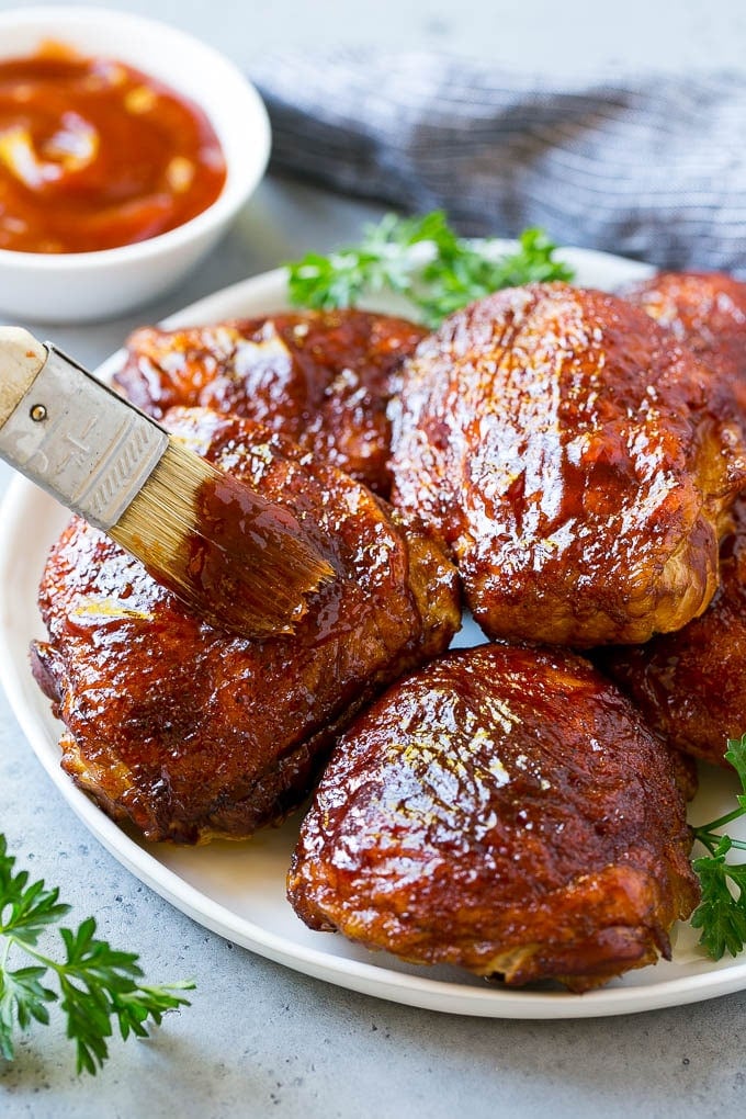 Smoked Chicken Thighs Recipe | Barbecue Chicken Thighs | Easy Chicken Thighs #chicken #barbecue #smoker #dinner #ezlod A plate of smoked chicken thighs being basted with barbecue sauce.