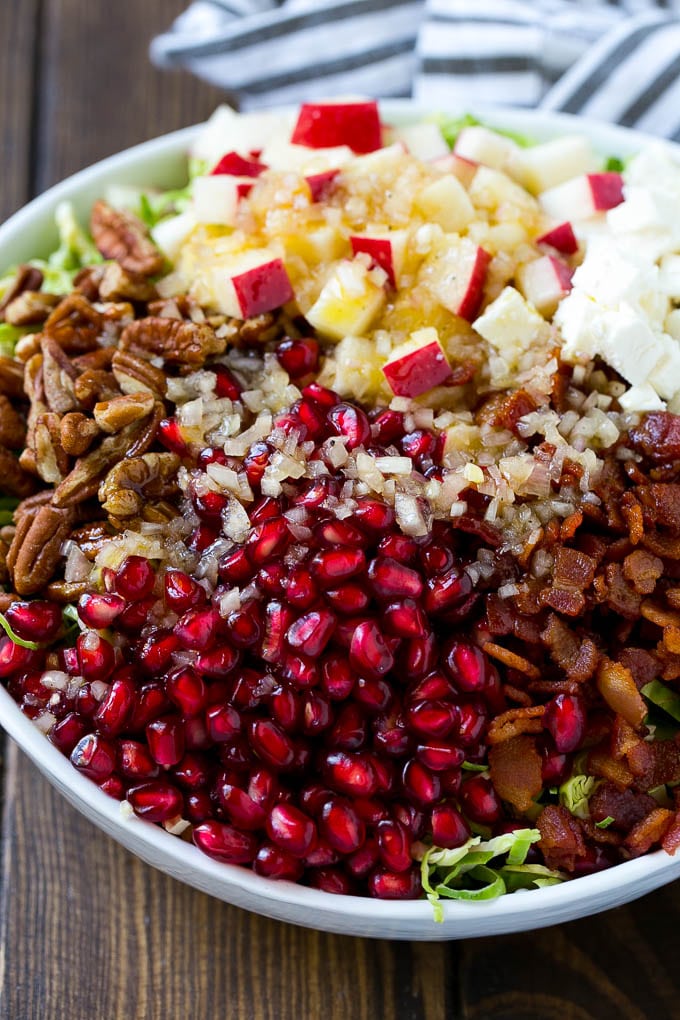 Brussels Sprout Salad Recipe | Shredded Brussels Sprouts Salad | Fall Salad #salad #brusselssprouts #bacon #thanksgiving #pomegranate #apple #dinner #ezlod Dressing poured on top of salad that contains sprouts, pomegranate seeds, pecans and bacon.