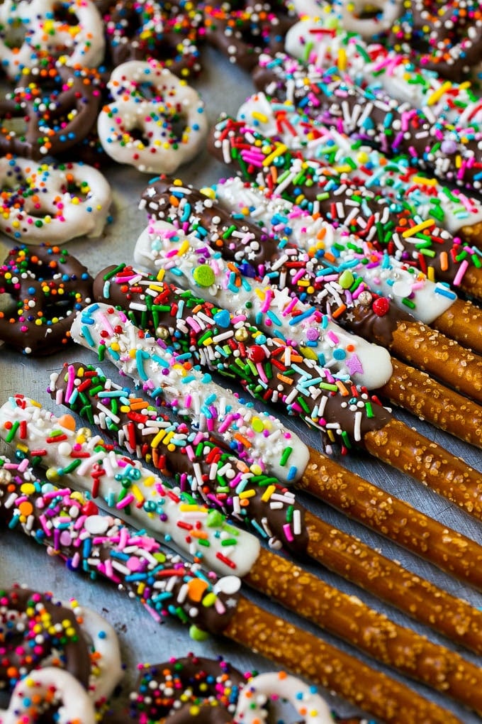 Chocolate Covered Pretzels Recipe | Sprinkle Pretzels | No Bake Dessert #pretzels #chocolate #christmas #sprinkles #candy #ezlod A sheet pan with coated twists and rods decorated with rainbow sprinkles.