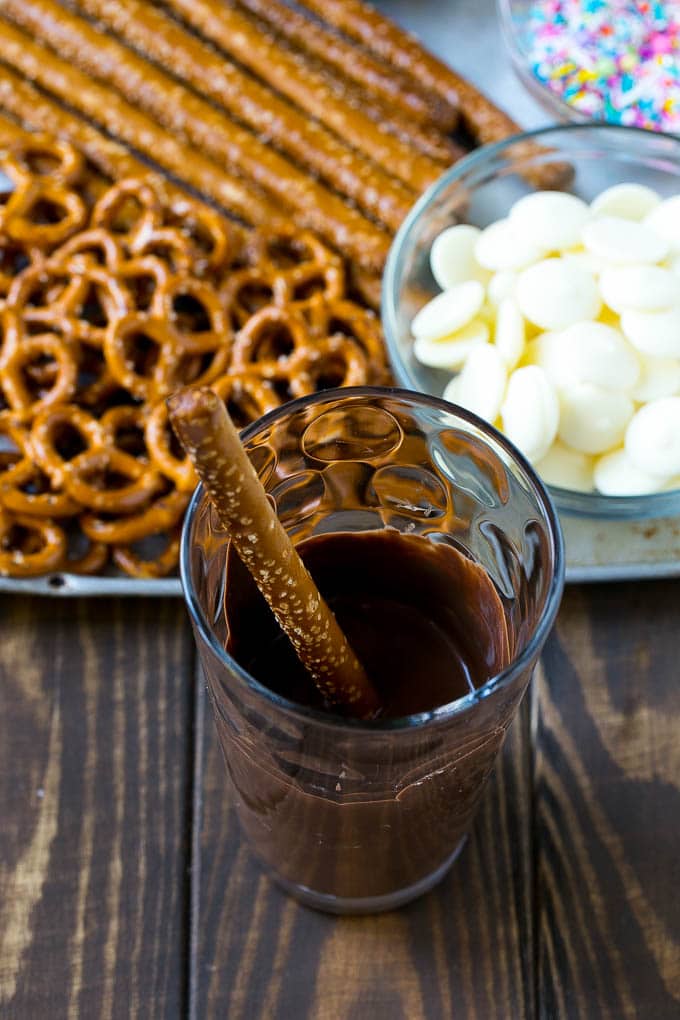 Chocolate Covered Pretzels Recipe | Sprinkle Pretzels | No Bake Dessert #pretzels #chocolate #christmas #sprinkles #candy #ezlod A rod in a glass full of melted chocolate.