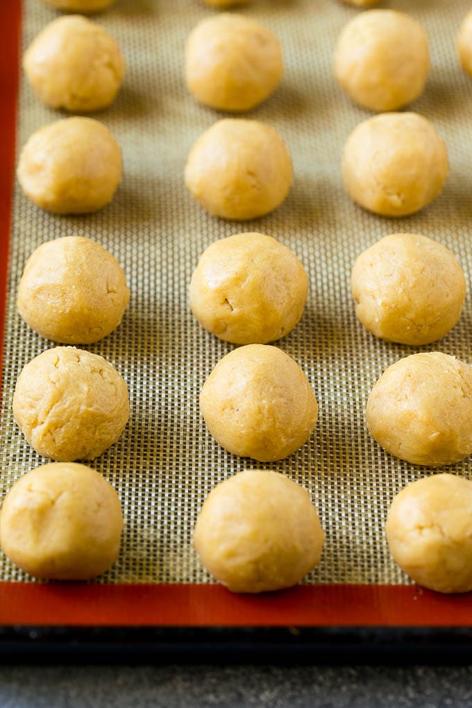 Peanut Butter Blossoms Recipe | Hershey Kiss Cookies | Chocolate Peanut Butter Cookies #cookies #peanutbutter #chocolate #dessert #baking #christmas #christmascookies #ezlod Balls of dough on a baking sheet.