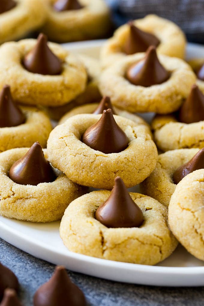 Peanut Butter Blossoms Recipe | Hershey Kiss Cookies | Chocolate Peanut Butter Cookies #cookies #peanutbutter #chocolate #dessert #baking #christmas #christmascookies #ezlod A plate with peanut butter blossoms stacked onto it.
