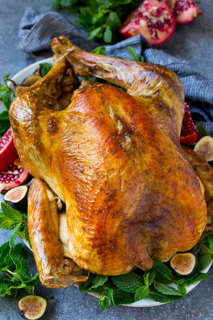 Roast Turkey Recipe | Thanksgiving Turkey | Holiday Turkey | Baked Turkey #turkey #thanksgiving #christmas #dinner #glutenfree #ezlod A Thanksgiving roast turkey on a serving platter garnished with herbs, pomegranate and figs.