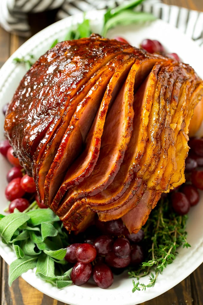 Brown Sugar Smoked Ham Recipe | Holiday Ham Recipe | Brown Sugar Glazed Ham #ham #christmas #thanksgiving #easter #smoker #dinner #brownsugar #ezlod #glutenfree A brown sugar glazed smoked ham on a serving platter surrounded by grapes and fresh herbs.