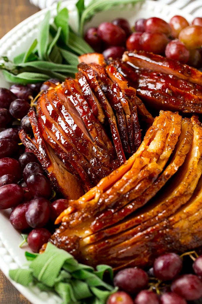 Brown Sugar Smoked Ham Recipe | Holiday Ham Recipe | Brown Sugar Glazed Ham #ham #christmas #thanksgiving #easter #smoker #dinner #brownsugar #ezlod #glutenfree Sliced smoked ham on a serving platter, garnished with grapes and fresh herbs.