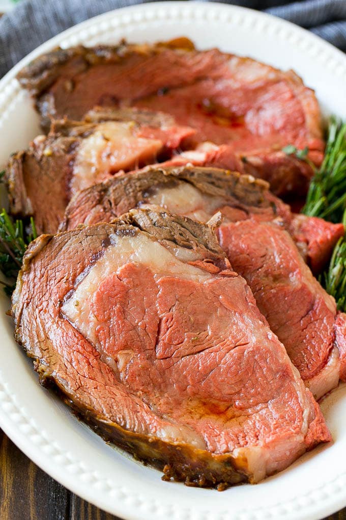 Smoked Prime Rib Recipe | Easy Prime Rib | Smoked Beef | Holiday Prime Rib #primerib #beef #smoker #dinner #ezlod #christmas #thanksgiving #lowcarb #keto Slices of beef garnished with fresh herbs.