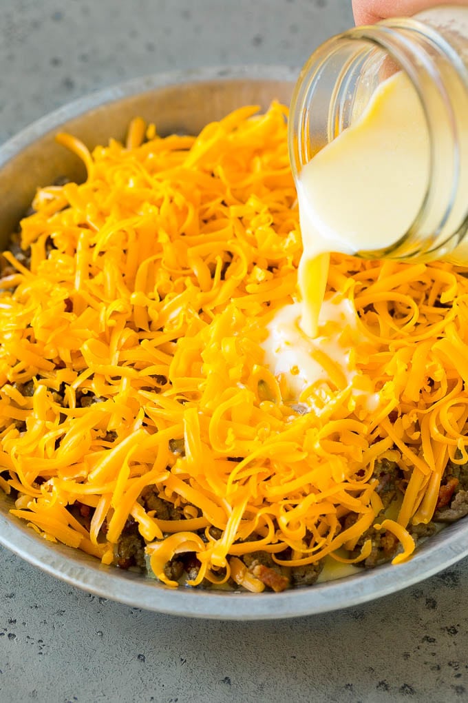 Cheeseburger Pie Recipe | Cheeseburger Casserole | Ground Beef Recipe #cheeseburger #beef #bacon #cheese #casserole #dinner #ezlod Egg batter being poured over shredded cheese and ground beef.