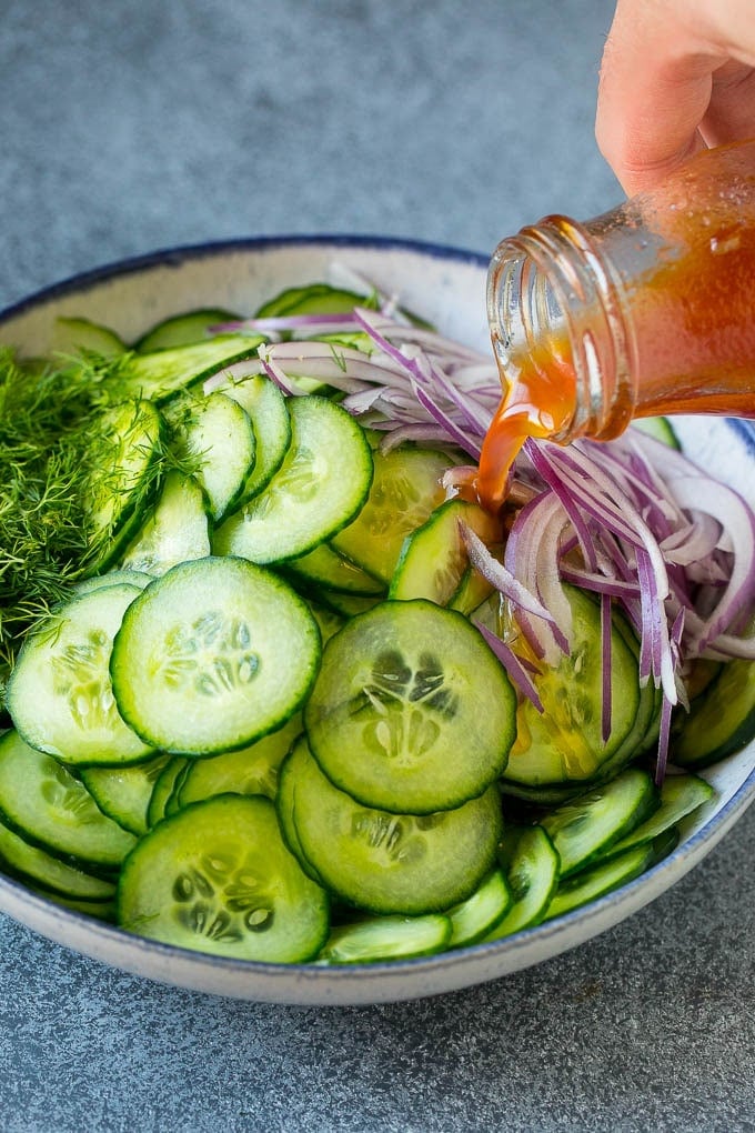 Cucumber Salad Recipe | Cucumber Dill Salad | Cucumber Recipe #cucumbers #salad #glutenfree #sidedish #ezlod Dressing being poured over sliced vegetables and fresh dill.