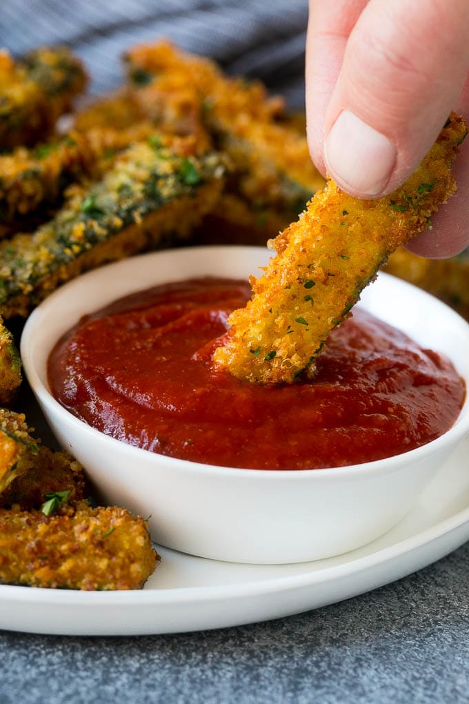 Fried Zucchini Recipe | Zucchini Fries | Zucchini Recipe #appetizer #zucchini #snack #ezlod A hand dipping a piece of fried zucchini into marinara sauce.