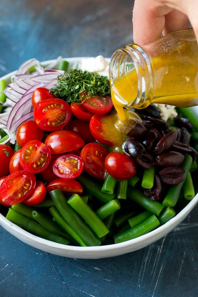 Green Bean Salad Recipe | String Bean Salad | Chopped Salad #greenbeans #tomatoes #olives #salad #cleaneating #lowcarb #glutenfree #ezlod Dressing being poured over veggies like cherry tomatoes, olives and onions.