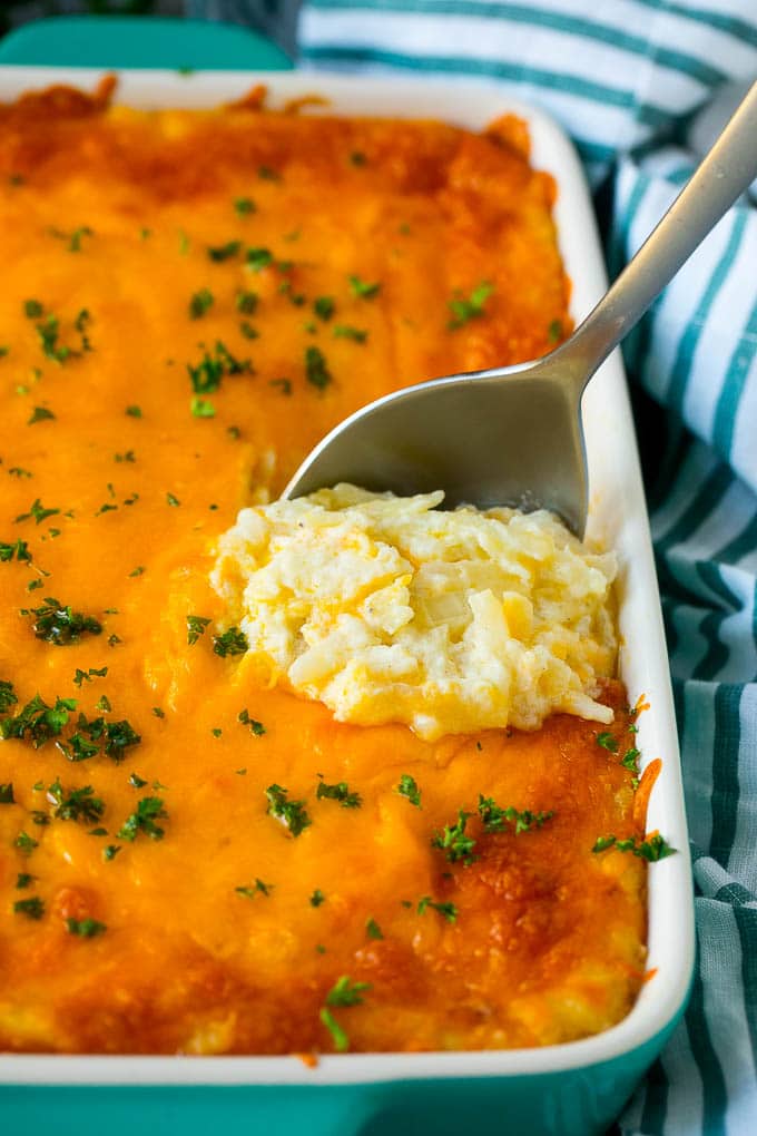 Hash Brown Casserole | Potato Casserole | Hash Brown Side Dish #potatoes #cheese #casserole #sidedish #ezlod Hash brown casserole with potatoes, cheddar cheese, onions and sour cream, with a serving spoon in the dish.