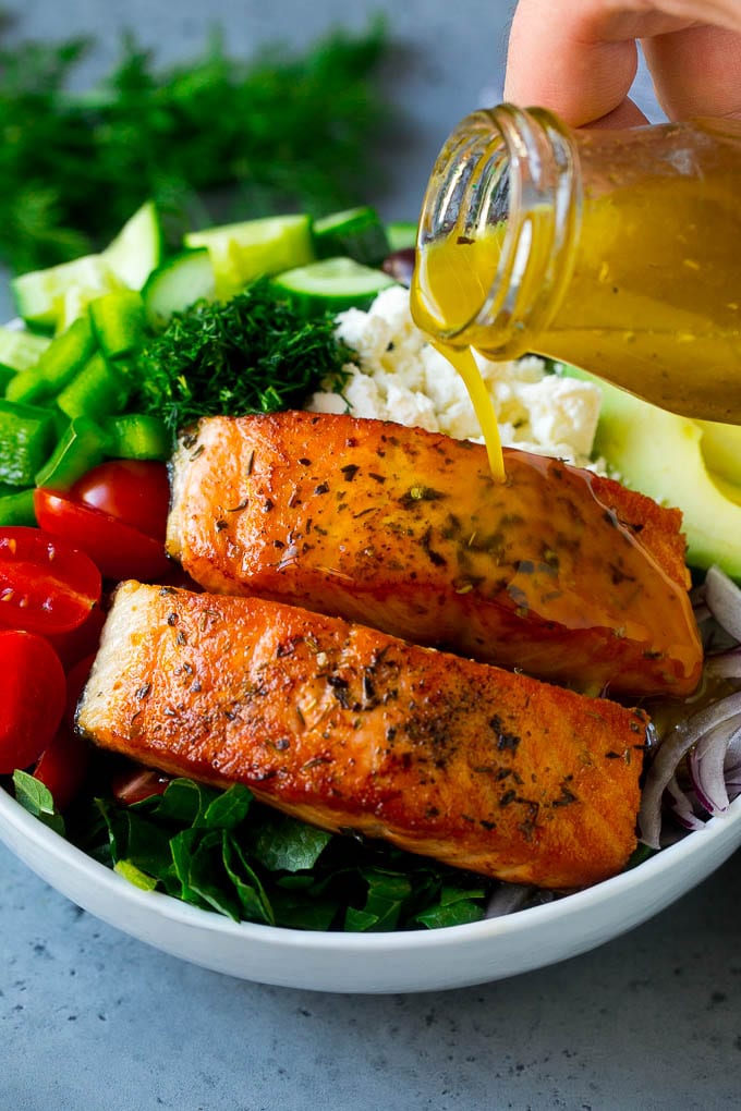 Greek Salmon Salad Recipe | Low Carb Salmon Recipe | Salmon Salad #salmon #seafood #fish #lowcarb #keto #lunch #ezlod #healthy Salmon fillets on top of greens with dressing being poured over the top.