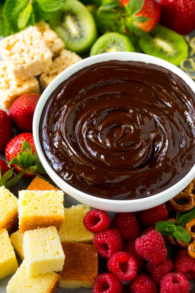 Chocolate Fondue Recipe | Chocolate Sauce | Chocolate Dip #chocolate #dessert #glutenfree #fondue #ezlod A bowl of chocolate fondue surrounded by fruit, cake, rice krispy treats and pretzels.