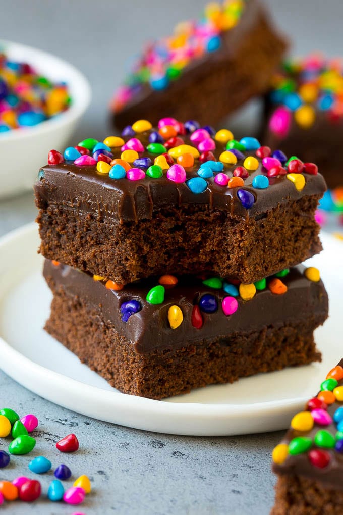 Cosmic Brownies Recipe | Cocoa Brownies | Frosted Brownies #brownies #chocolate #dessert #ezlod #sprinkles A stack of cosmic brownies on a plate with a bite taken out of one.