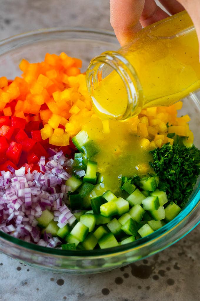 Israeli Salad Recipe | Cucumber Salad | Tomato Salad | Chopped Salad #salad #cleaneating #healthy #glutenfree #lowcarb #keto #sidedish #lunch #ezlod Lemon dressing being poured over chopped vegetables.