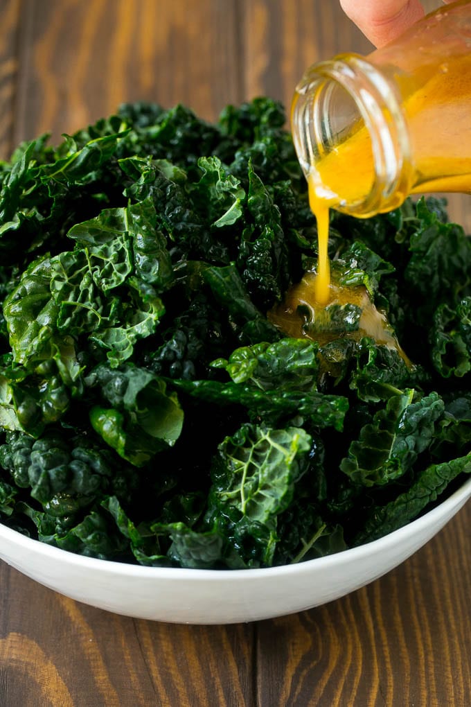 Apple Kale Salad Recipe | Kale Recipe | Fall Salad #kale #apples #bacon #salad #feta #dinner #lunch #ezlod Dressing being poured over dinosaur kale leaves.