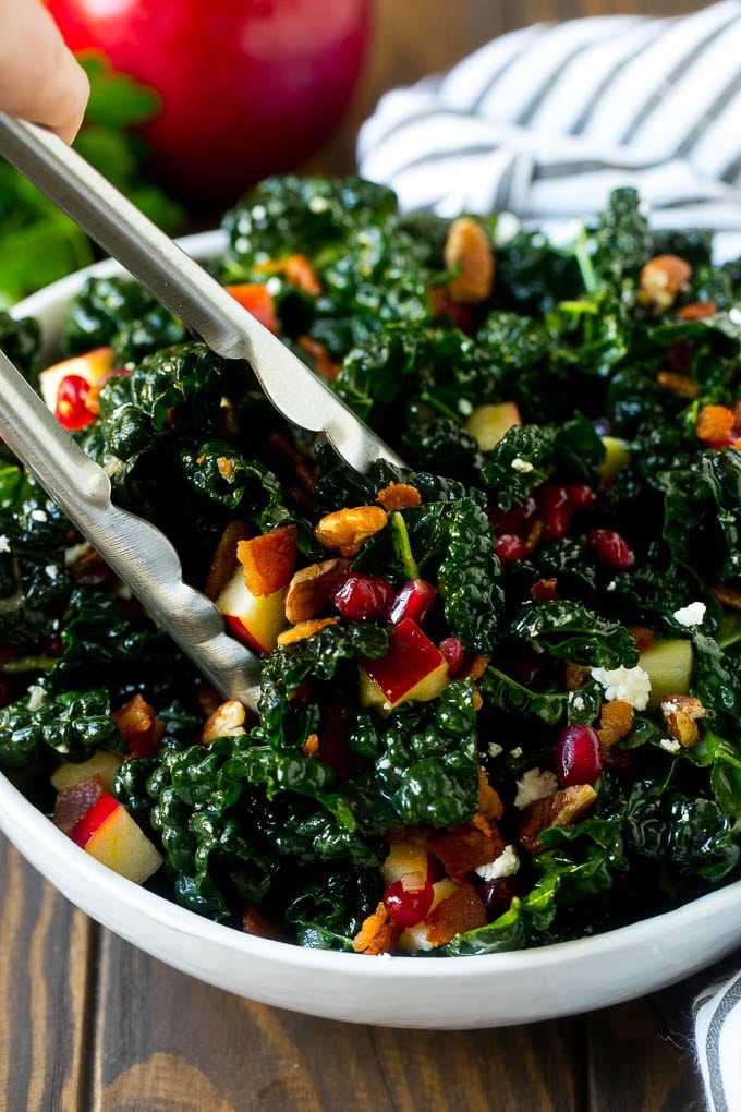 Apple Kale Salad Recipe | Kale Recipe | Fall Salad #kale #apples #bacon #salad #feta #dinner #lunch #ezlod Tongs in a bowl of kale and apple salad.