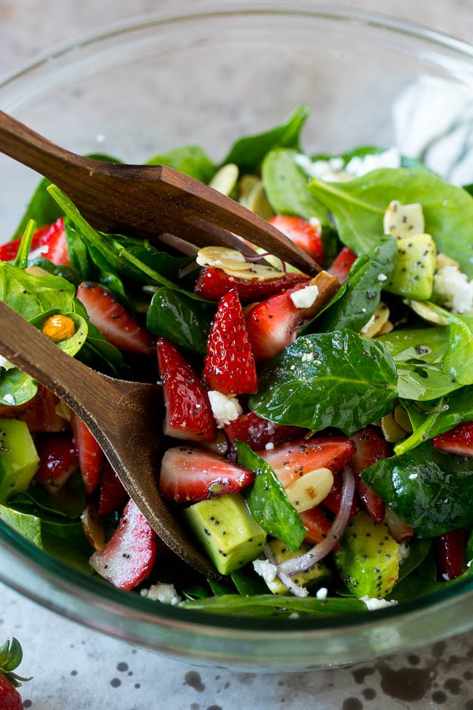 Strawberry Spinach Salad Recipe | Strawberry Salad | Spinach Salad #spinach #salad #strawberries #avocado #ezlod Salad tongs in a bowl of spinach salad with strawberries.