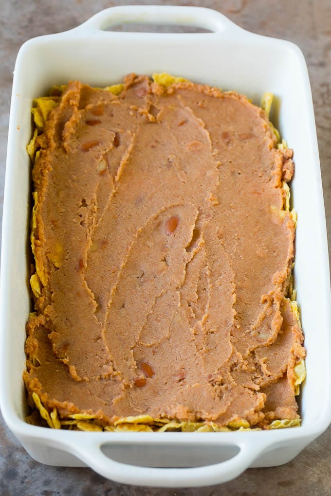 Taco Casserole Recipe | Mexican Casserole | Beef Casserole #casserole #tacos #beef #dinner #cheese #ezlod A layer of refried beans on top of a crushed tortilla chips.