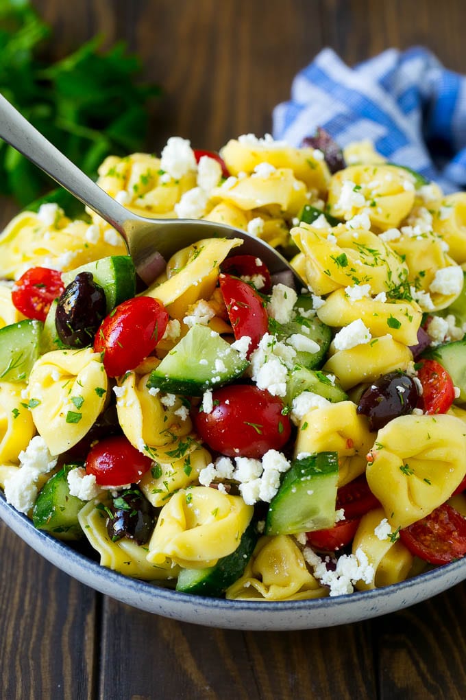 Greek Tortellini Salad Recipe | Pasta Salad | Tortellini Salad | Greek Salad #greek #tortellini #pasta #salad #cucumbers #olives #dinner #ezlod A bowl of Greek tortellini salad with a serving spoon in it.