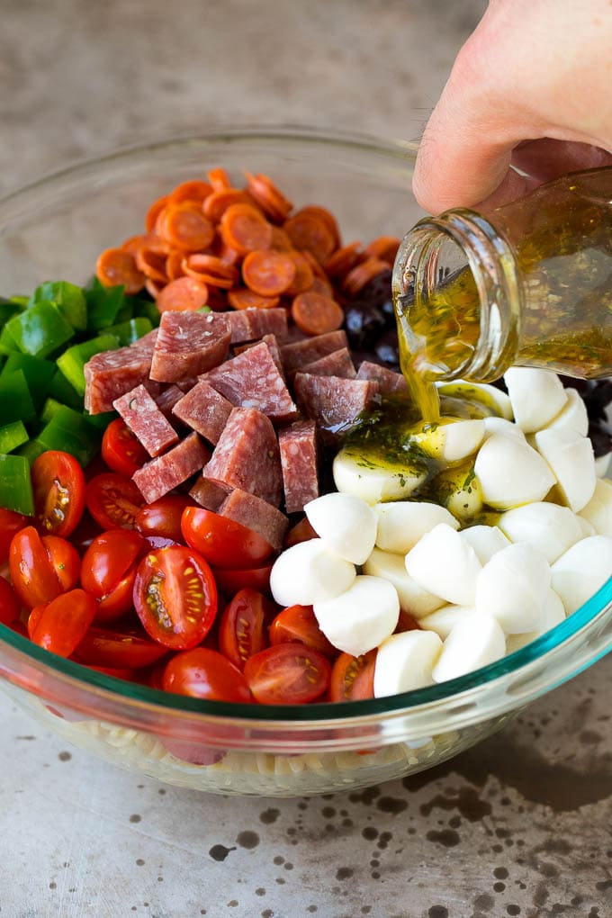 Italian Pasta Salad | Pasta Salad Recipe #pasta #salad #pastasalad #pepperoni #salami #olives #cheese #sidedish #ezlod Italian dressing being poured over pasta salad ingredients.